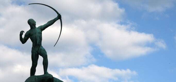 Image shows a statue of an archer against a blue sky.