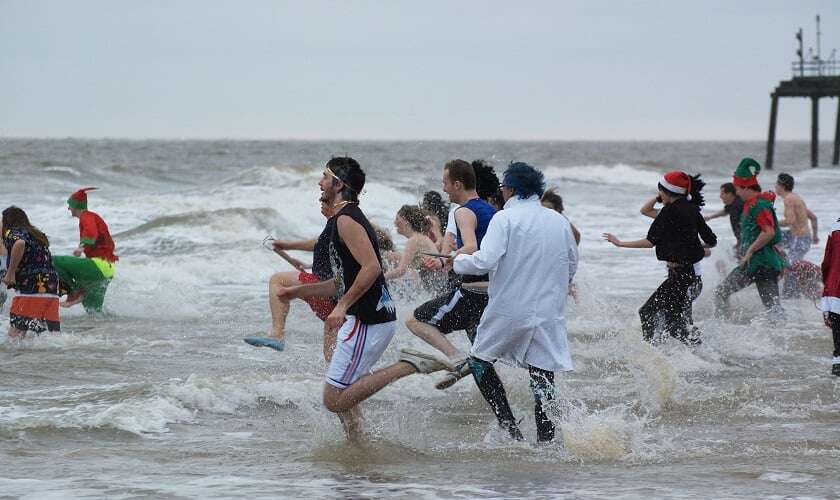 Image shows people running into a cold sea, some of them in fancy dress.