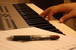 Image shows someone at a piano composing music.