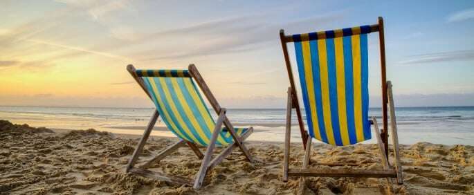Image shows two deckchairs on a beach at sunrise.