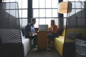 Image shows a woman showing a man something on a laptop, while he takes notes.