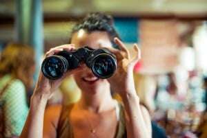 Image shows a young woman looking through binoculars. 