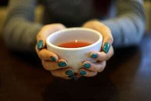 Image shows someone holding out a cup of tea.