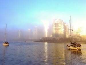 Image shows boats sailing towards a fog-shrouded city. 
