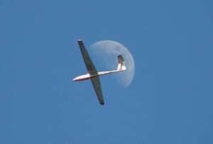 Image shows a glider flying in front of the moon. 