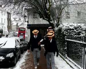 Image shows Harrow pupils, complete with straw hats, walking near the school in the snow. 