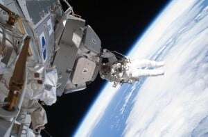 Image shows the International Space Station beside the curvature of the Earth, with an astronaut on the outside.