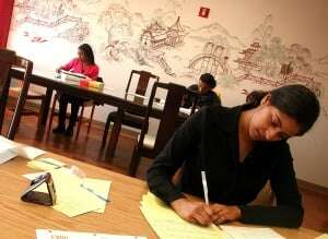 Image shows three students at separate desks, studying independently.