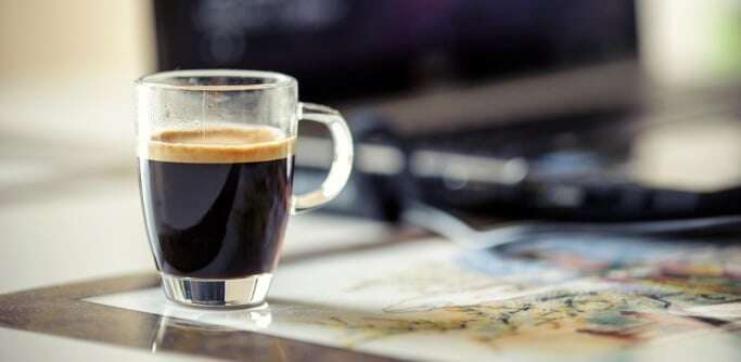Image shows an espresso next to a laptop on a desk.