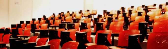 Image shows rows of red seats in a lecture theatre.
