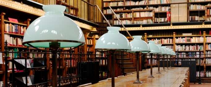 Image shows a row of old-fashioned lamps on a library table.