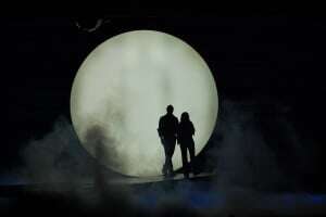 Image shows a moment in the musical 'Mamma Mia', with two characters silhouetted in front of the full moon. 