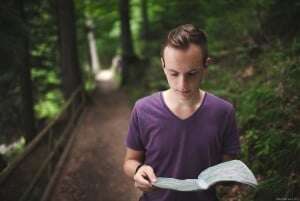 Image shows a young man holding a map in a forest.