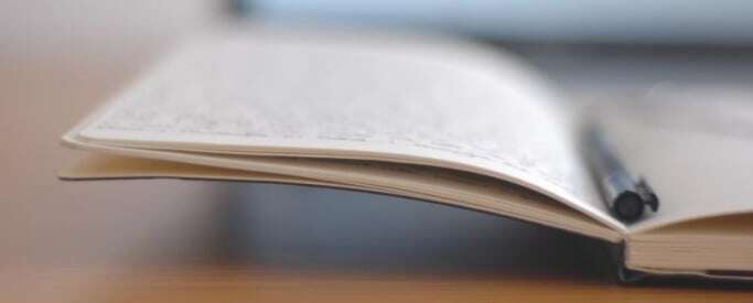 Image shows an open notebook with a pen resting on it.