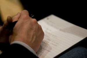 Image shows someone taking notes on a lined piece of paper.