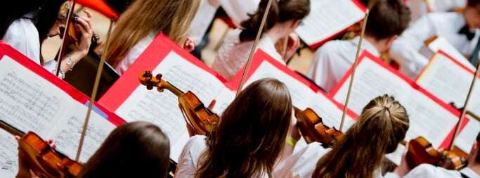 Image shows a row of violin players in an orchestra.