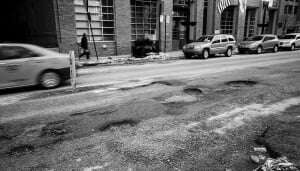 Image shows a road full of potholes.