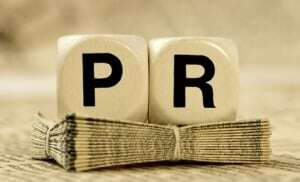 Image shows two dice, reading 'PR', on a stack of papers.