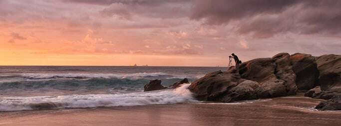 Image shows a photographer taking a photo on a beach at sunset.