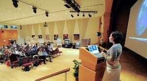 Image shows a woman giving a presentation.