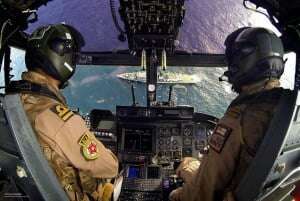 Image shows RAF pilots in a helicopter with its nose dipped towards a ship.