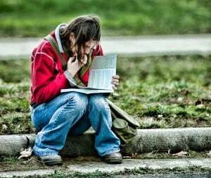 Image shows a teenage girl reading a textbook on a kerb.
