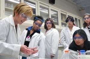 Image shows school students watching a scientist in a lab.