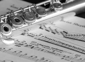 Image shows a flute lying on top of some sheet music, in black and white.