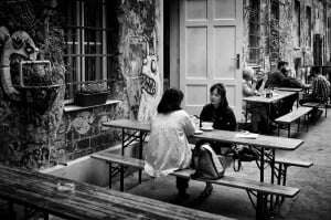 Image shows two women on a bench outside a cafe, talking.