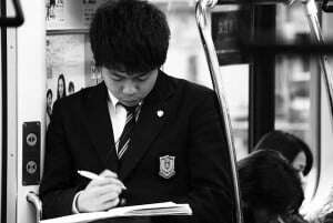 Image shows a student in a school uniform making notes on a train.