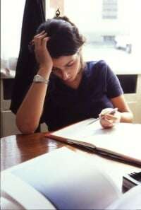 Image shows a young woman studying, resting her head on one hand.
