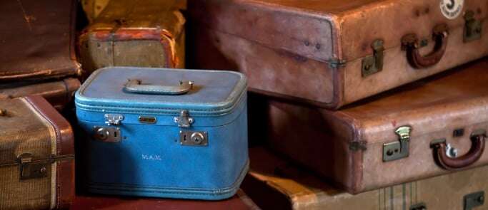 Image shows a pile of old-fashioned suitcases, including one small blue one in the foreground.