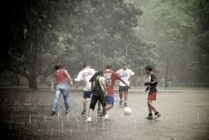 Image shows a group of teenagers playing football in the rain.