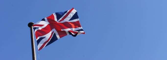 Image shows a Union Jack flying against a clear blue sky.
