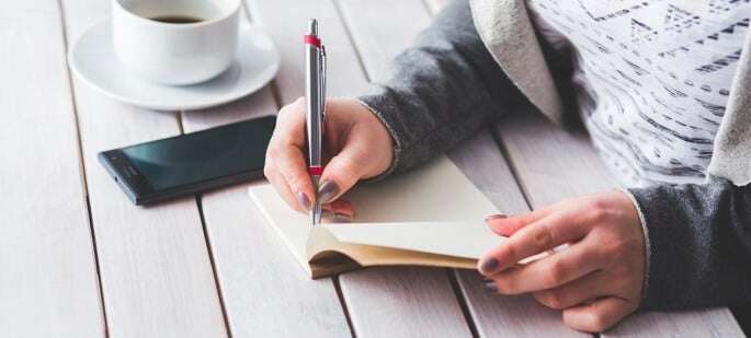 Image shows a woman writing in a notebook.