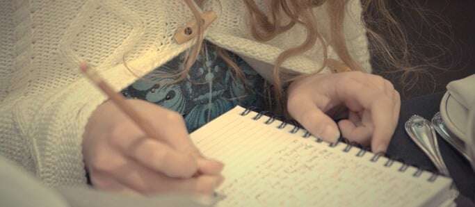 Image shows someone writing in a notebook.