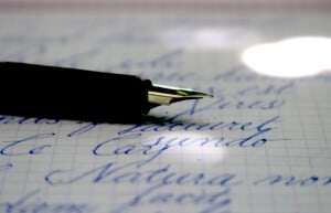 Image shows a fountain pen on top of a piece of paper with beautiful calligraphy. 