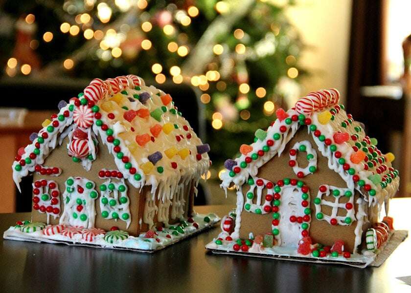 Two gingerbread houses sit on a table near a Christmas tree. 