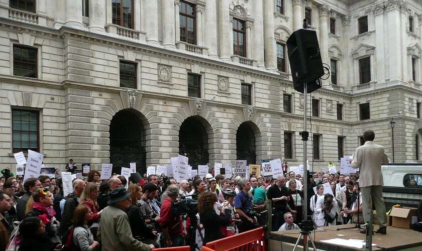 Image shows Blakemore on a makeshift stage addressing a crowd with placards. 