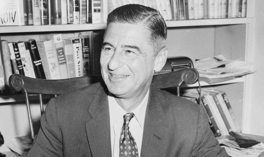 Image shows Dr Seuss, smiling, with a bookcase behind him.