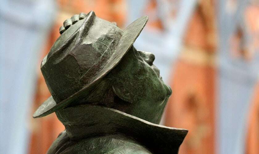 Image shows a copper statue of Betjeman looking up at the roof of St Pancras, and holding on to his hat.