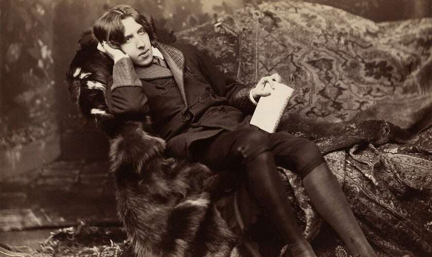 Image shows a black-and-white photo of Oscar Wilde lounging on a sofa.
