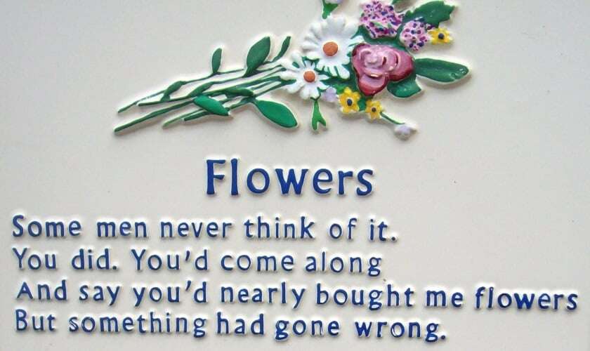 Image shows metal plaque with the first verse of the poem 'Flowers'. 